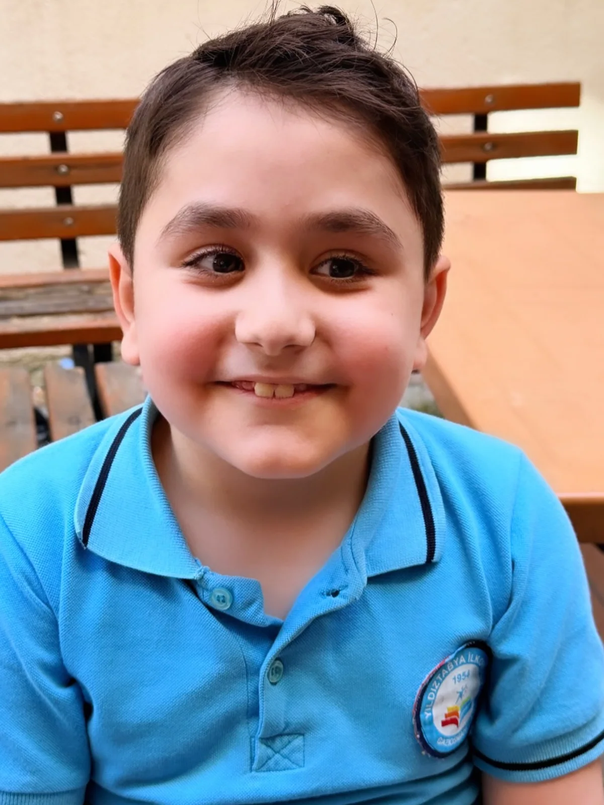 Ahmet Yuşa mavi okul üstüyle masada gülümsüyor.